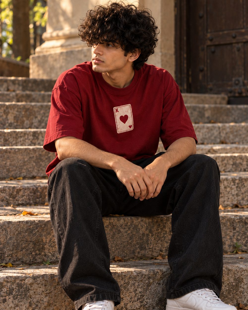 Face Card tee in maroon, heart card chest print, seated on worn stone steps