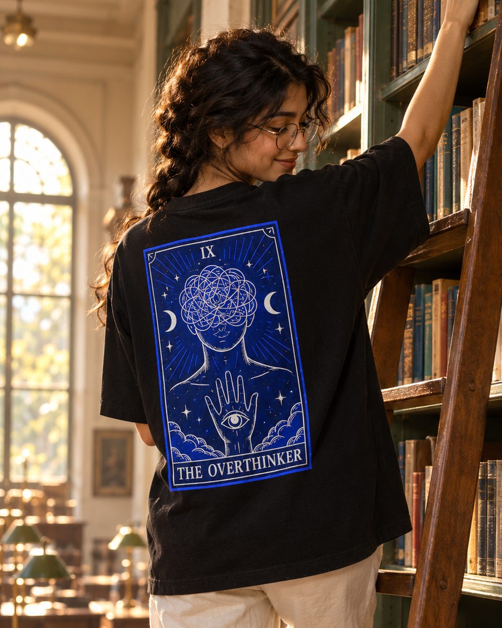 The Overthinker tee, tarot card IX back print, on a library ladder